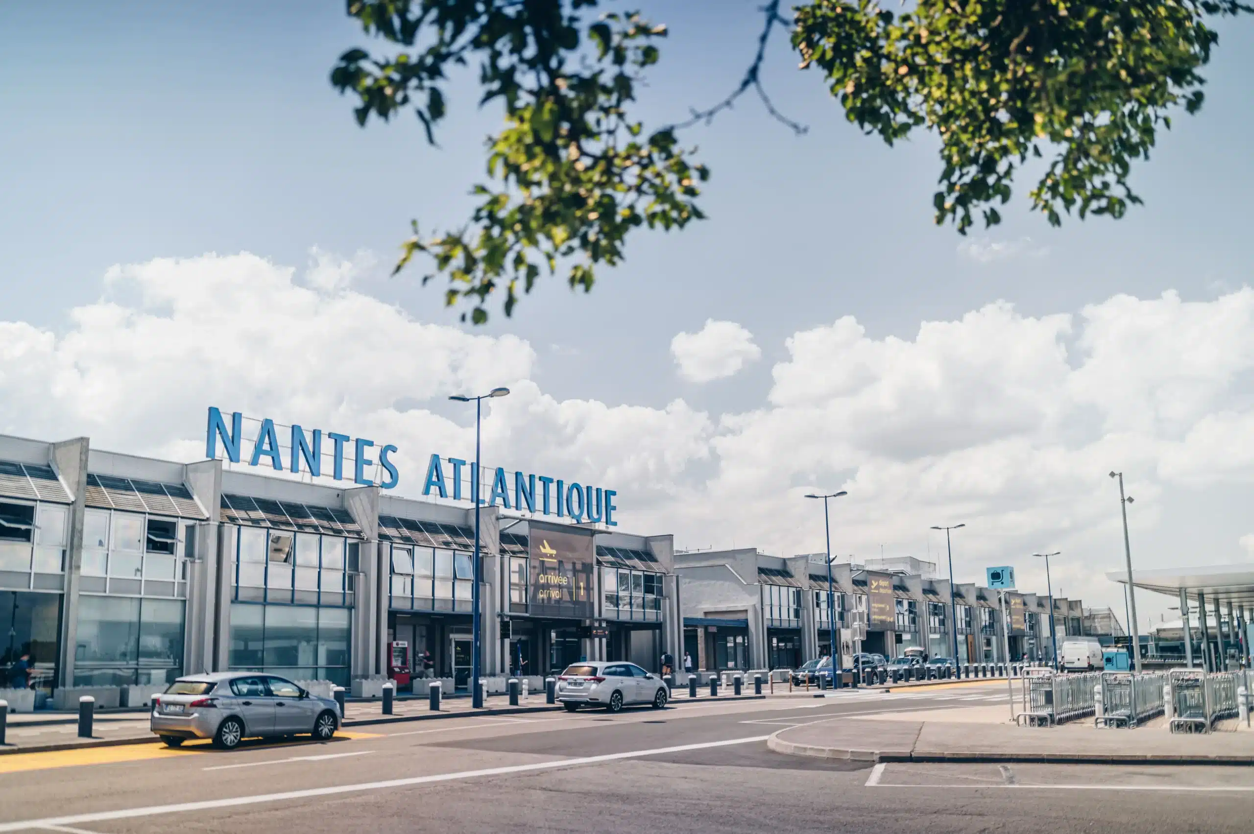 Façade principale de l'aéroport Nantes Atlantique sous un ciel bleu nuageux. Point d'entrée logistique majeur pour les agences événementielles étrangères, géré par l'Agence Helper, DMC bilingue expert en Loire-Atlantique